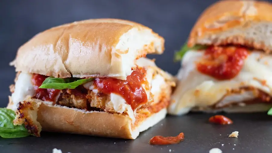 Chicken parmigiana sandwich on a roll with sauce and basil